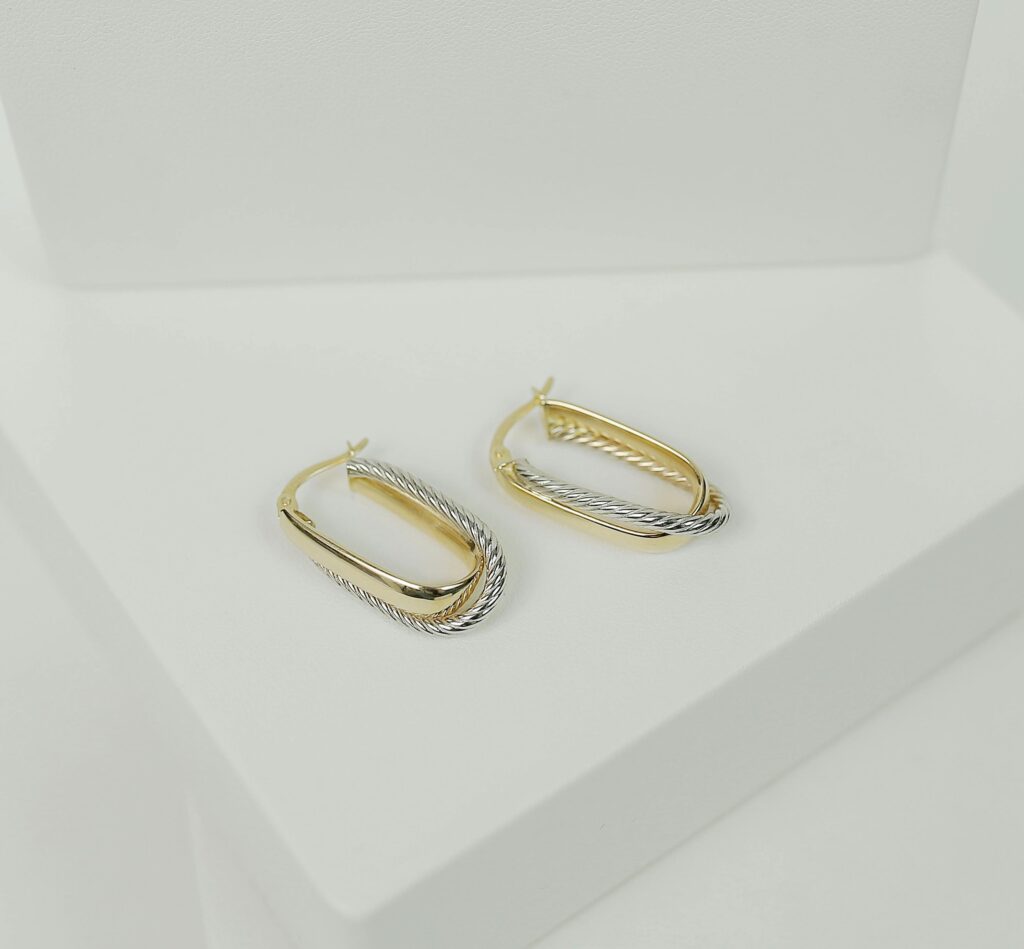 A stylish pair of gold and silver earrings showcased on a white surface, ideal for elegant occasions.